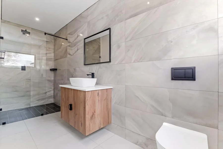 Helderfontein bathroom with marble-look wall tiles, glass shower, wood vanity, basin and mirror.