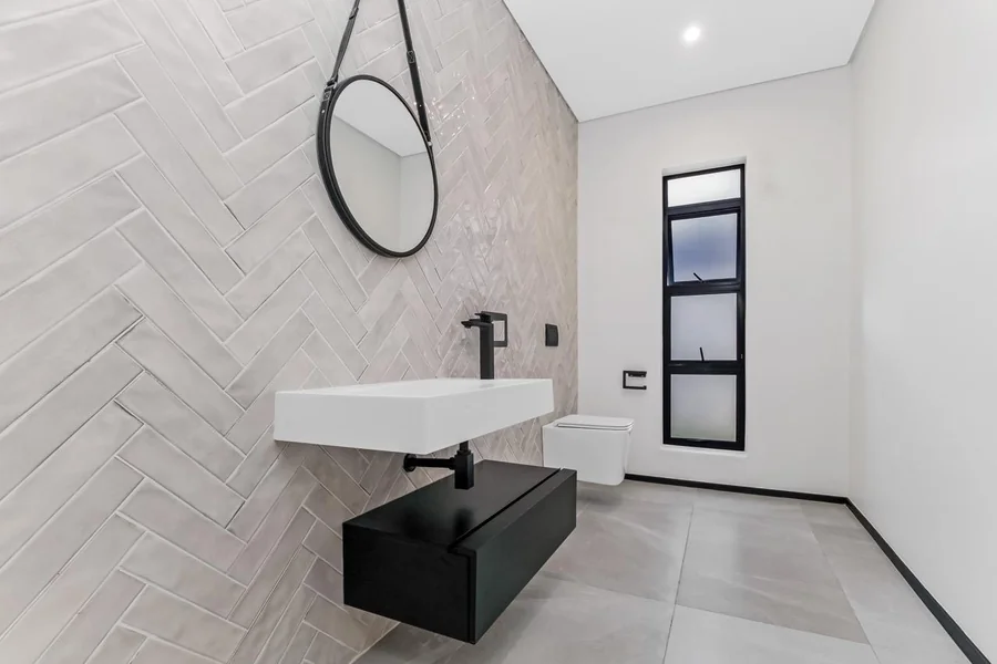 Helderfontein bathroom with herringbone wall tiling, floating black vanity, vessel sink and black-framed window.