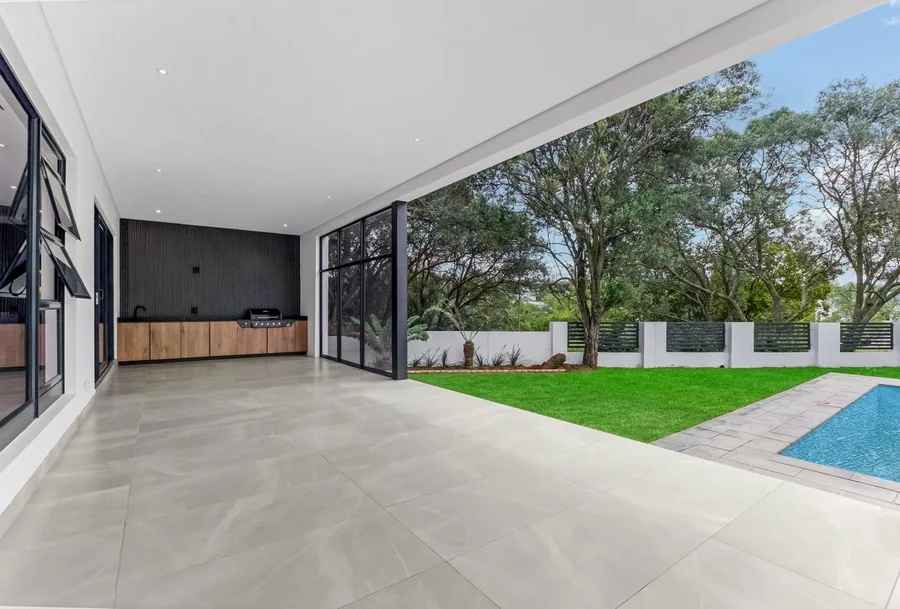 Helderfontein covered outdoor patio with built-in barbecue, manicured lawn, mature trees and swimming pool.